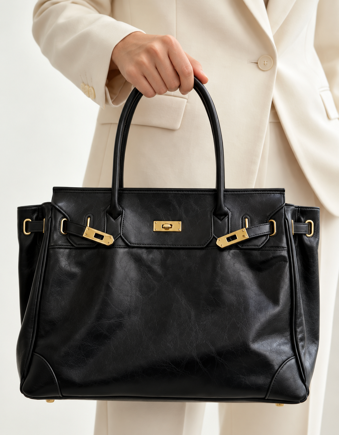 Sac à main noir en cuir de luxe de Danoir Paris, fait main, posé sur un costume ivoire, élégant et sophistiqué.