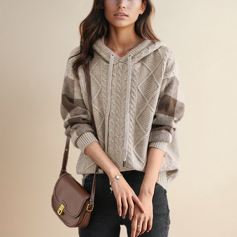 Pull à capuche Emily de la collection #1752 de Danoir Paris, en tricot tressé gris clair, porté avec une poche kangourou.