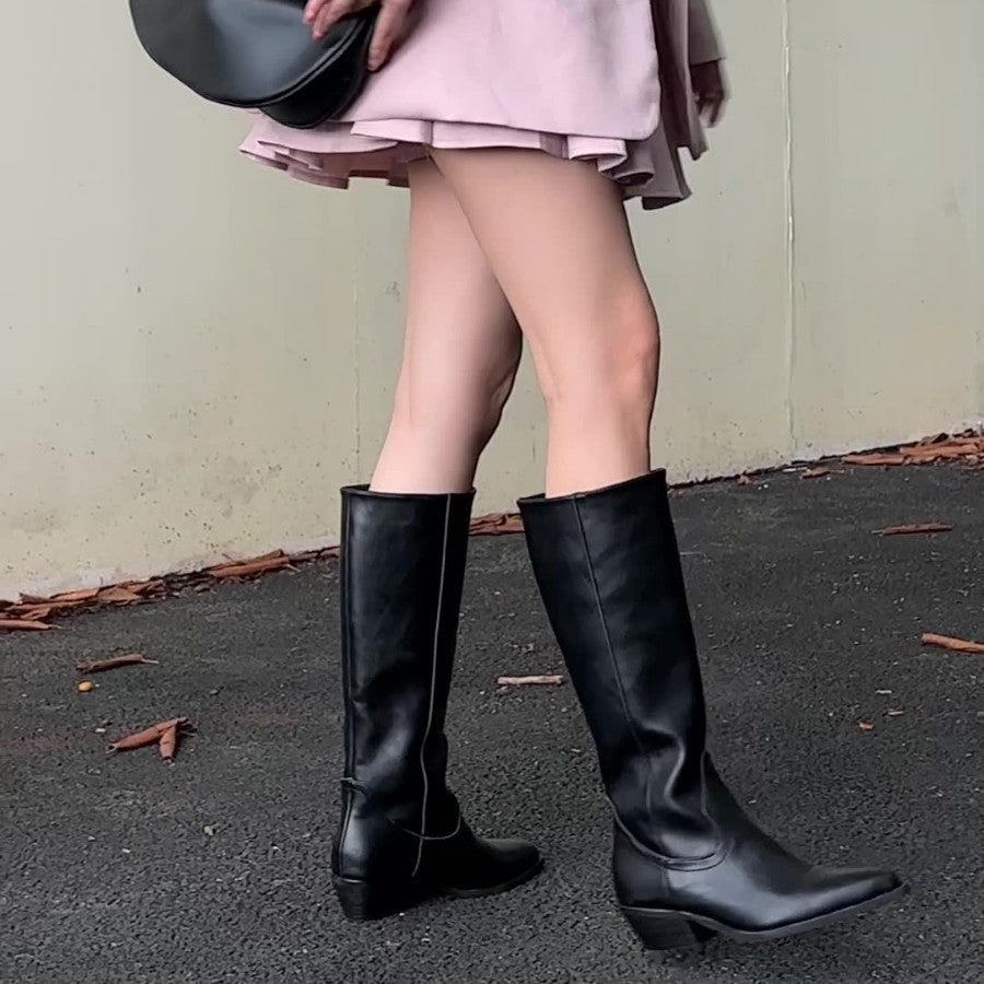 Bottes hautes Danoir Paris Aurélie avec bout pointu, en cuir noir, sur une femme debout dans une rue urbaine.
