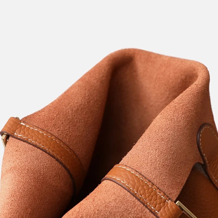 Sac seau orange Portico de Danoir Paris, en cuir, avec poignée et fermeture métallique, posé sur une surface claire.